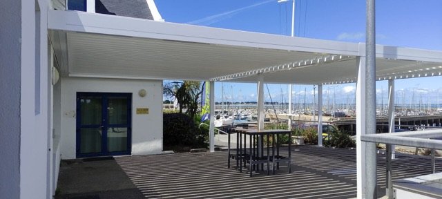 Grande pergola bioclimatique blanche couvrant la terrasse d'un club nautique sur le port de Quiberon
