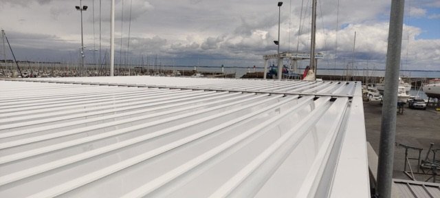 Lames fermées de la grande pergola du club nautique, avec le port en fond